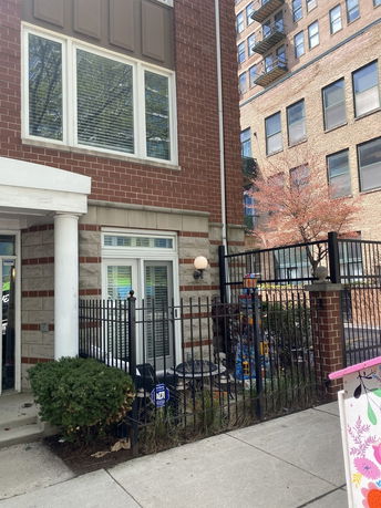 Front view of a multi-story brick building with large windows and a fenced entryway.