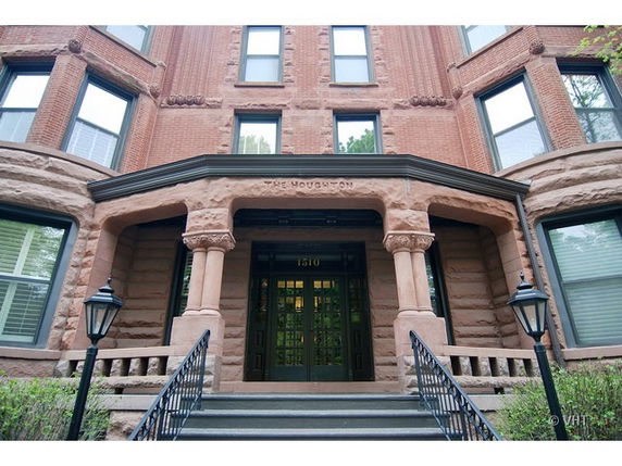 Front view of a brick building entrance with a stone archway and steps.