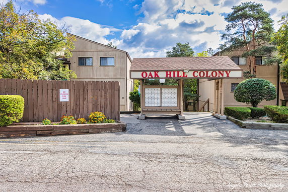 Front view of a residential building complex with an entrance sign reading 'Oak Hill Colony.'