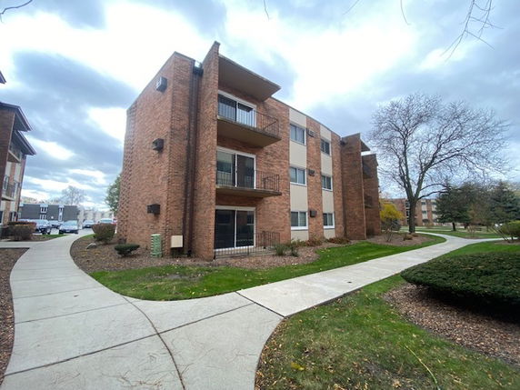 Front view of a three-story brick apartment building with balconies.