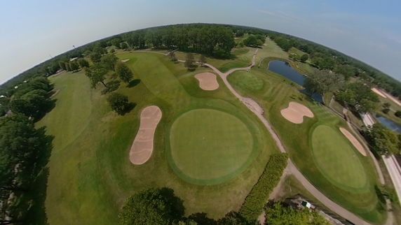 Aerial panoramic view of a golf course with green fairways, sand bunkers, and surrounding trees.