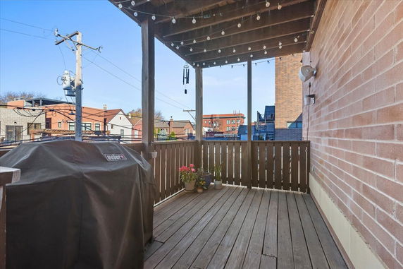 Rooftop with wooden flooring and string lights, featuring a covered barbecue grill and potted plants.
