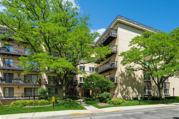Front view of a multi-story apartment building with balconies and surrounding trees.