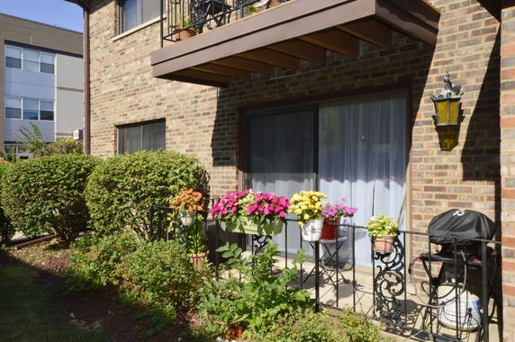 Exterior view of a residential building with a patio featuring potted flowers and a sliding glass door.