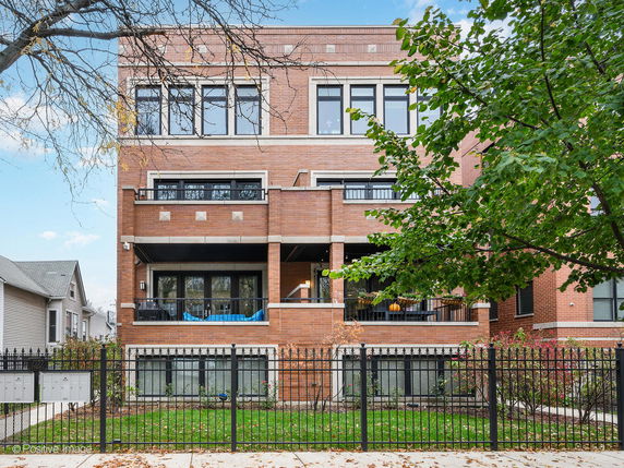 Front view of a multi-story brick building with balconies and black metal fence.