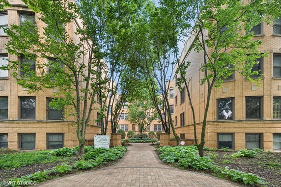 Front view of a multi-story brick apartment building with a pathway and trees.