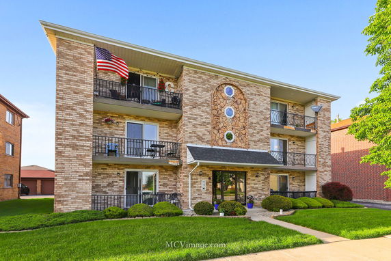 Front view of a three-story brick apartment building with balconies and large circular decorative windows.
