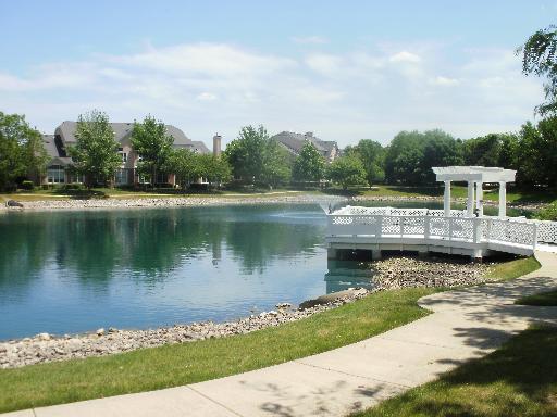 View of a pond with a white wooden dock and houses in the background.