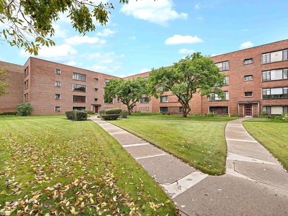 Front view of a multi-story brick building with multiple entrances and a walkway leading to the entrance.