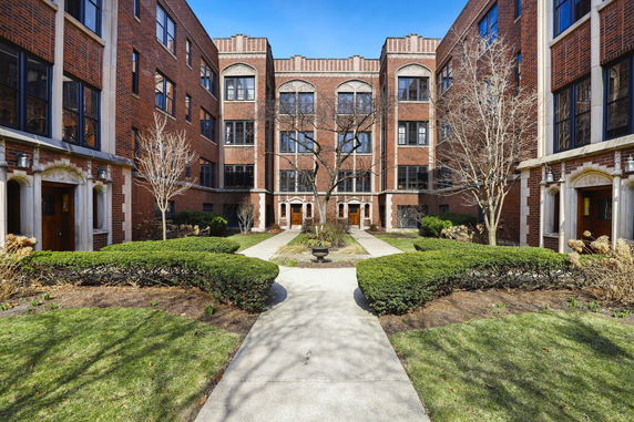 Front view of a red brick multi-story apartment building with a landscaped courtyard.