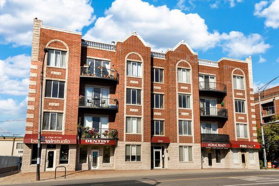 Front view of a multi-story brick building with balconies and ground-floor businesses.