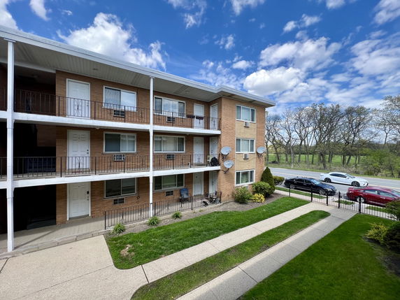Front view of a three-story brick apartment building with balconies.