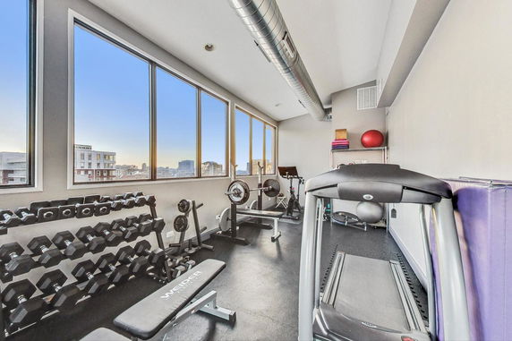 Indoor gym with exercise equipment and large windows.