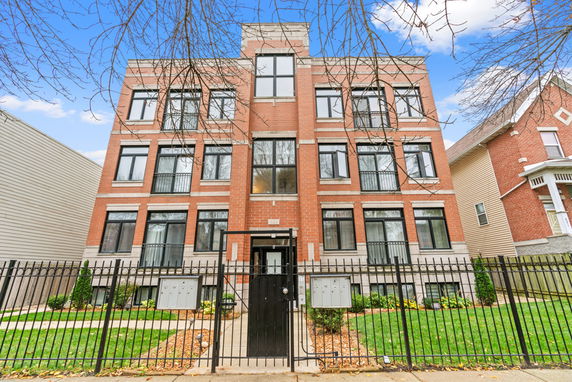 Front view of a multi-story brick building with large windows and a fenced front yard.