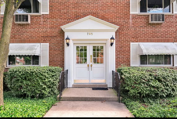 Front view of a brick building entrance with white double doors and outdoor lanterns.