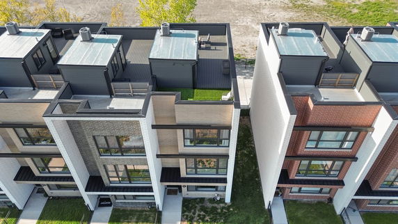 Aerial view of a row of modern townhouses with flat rooftops featuring chimneys and small structures.