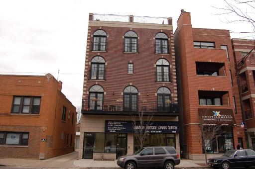 Front view of a multi-story brick building with arched windows and retail space on the ground floor.