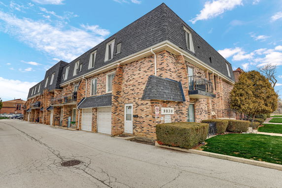 Front view of a multi-story brick residential building with garages and balconies.