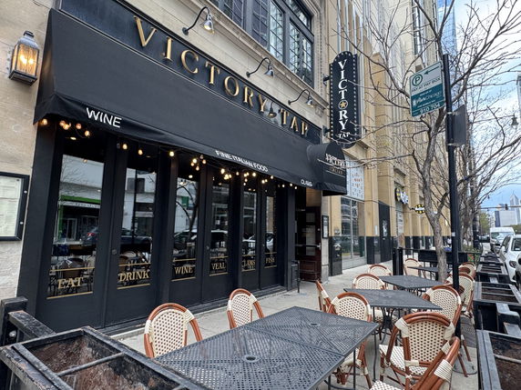 Street view of a restaurant with outdoor seating and a black awning.