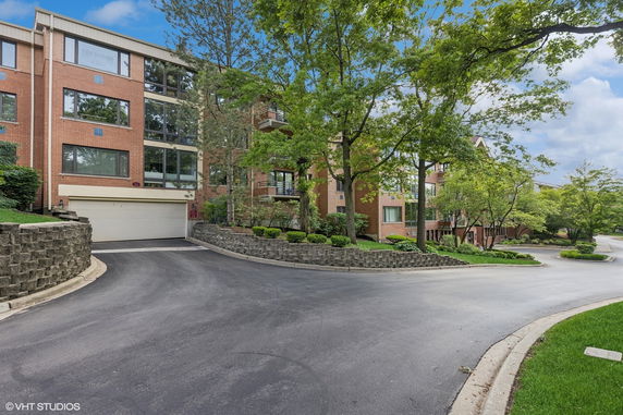 Front view of a modern multi-story brick building with large windows and a driveway.