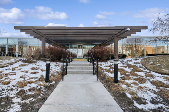 Front view of a building with large glass windows and a wooden pergola entrance.