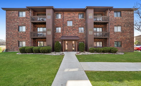Front view of a four-story brick apartment building with balconies.