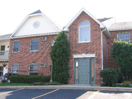 Front view of a brick two-story building with a gabled roof and arched window above the entrance.