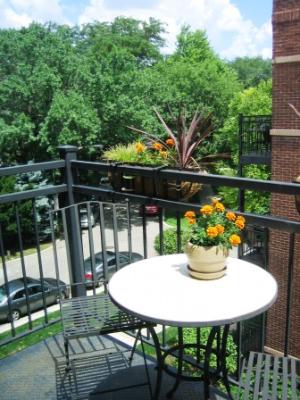 Outdoor balcony with a round table and chairs overlooking trees and parked cars.