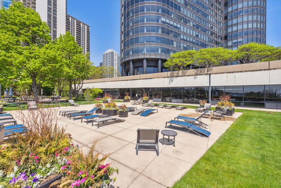 View of a modern high-rise building with a large outdoor patio area featuring lounge chairs and planters.