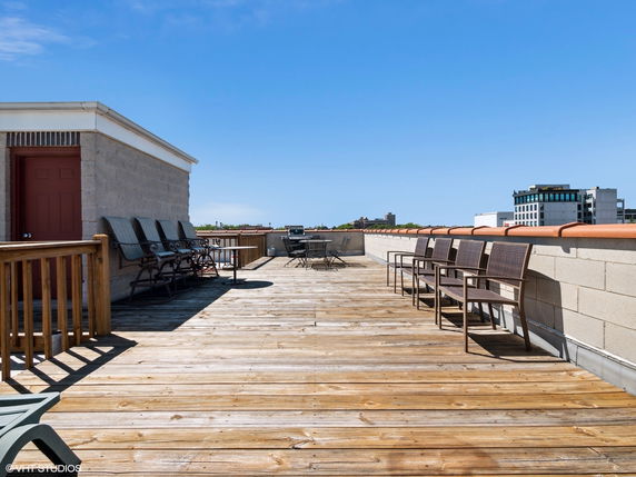 Rooftop with chairs and seating area, blue sky above.