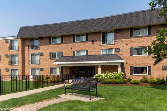 Front view of a three-story brick apartment building with a sloped roof and balconies.