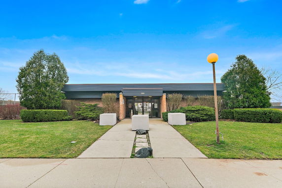 Front view of a single-story building with a glass entrance and surrounding greenery.