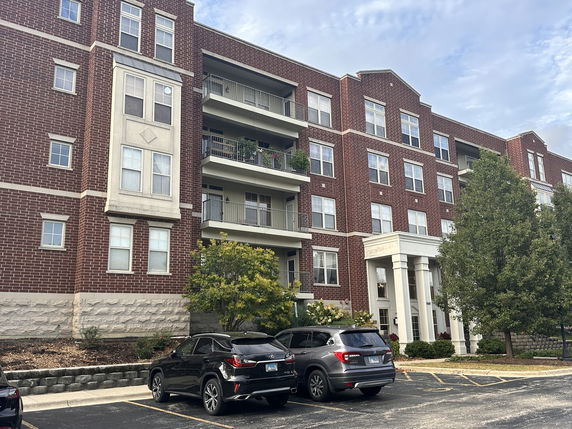 Front view of a multi-story red brick apartment building with balconies and parking area.