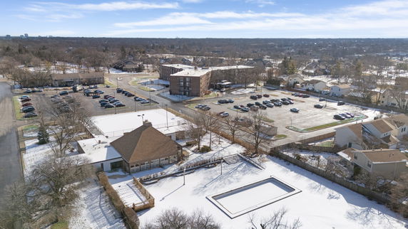 Panoramic view of a snow-covered area with buildings, parking lots, and surrounding residential neighborhoods.