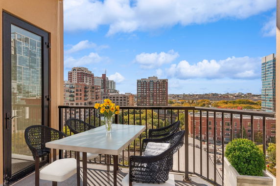Balcony with seating and a table overlooking urban buildings and a clear sky.
