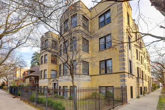 Front view of a multi-story brick apartment building with decorative windows and fenced frontage.