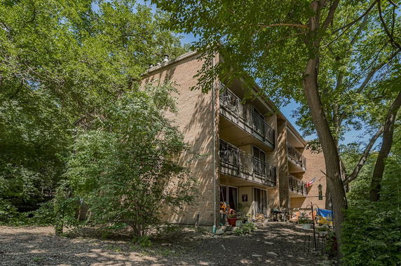 Exterior view of a three-story apartment building with balconies and surrounding trees.
