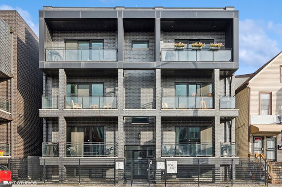 Front view of a modern multi-story building with balconies and glass railings.