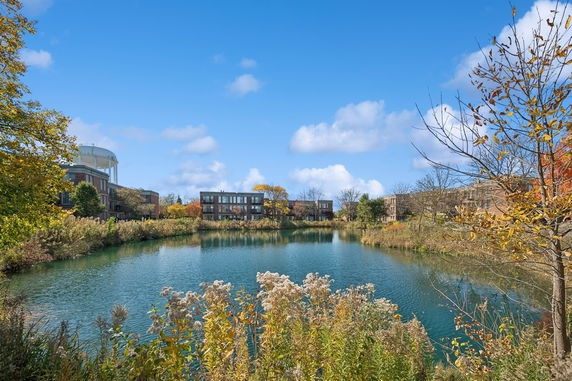View of a pond surrounded by buildings and trees under a clear blue sky.