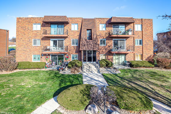 Front view of a three-story brick apartment building with balconies.