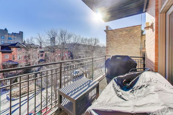 View from a balcony overlooking a street with brick buildings and trees.