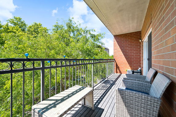 View from a balcony with outdoor seating and railings overlooking green trees and a distant building.
