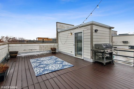Rooftop area with a wooden deck, a grill, and string lights.