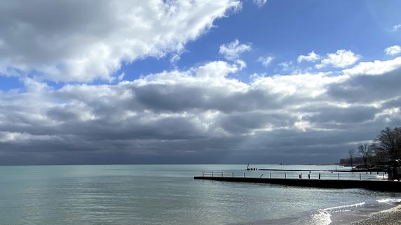 Panoramic view of a large body of water with a cloudy sky and trees in the distance.