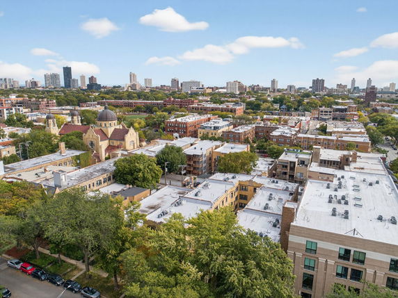 Panoramic view of a cityscape with various buildings and a large church with domes, surrounded by trees and a skyline in the distance.