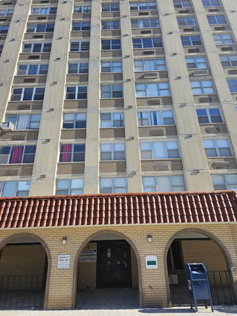 Front view of a multi-story apartment building with brick facade and arched entrance.