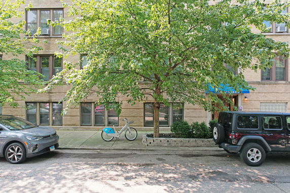 Front view of a multi-story brick building with multiple windows and a tree in front.