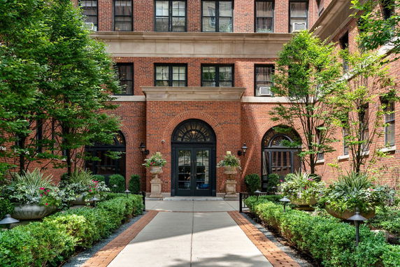 Front view of a brick multi-story building with arched entrances and decorative plants.