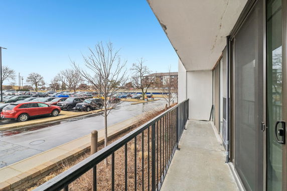 View from a balcony overlooking a parking area and nearby buildings.