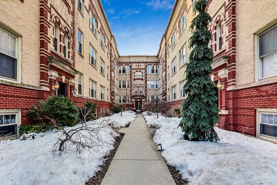Front view of a multi-story brick apartment building with snow-covered pathway.